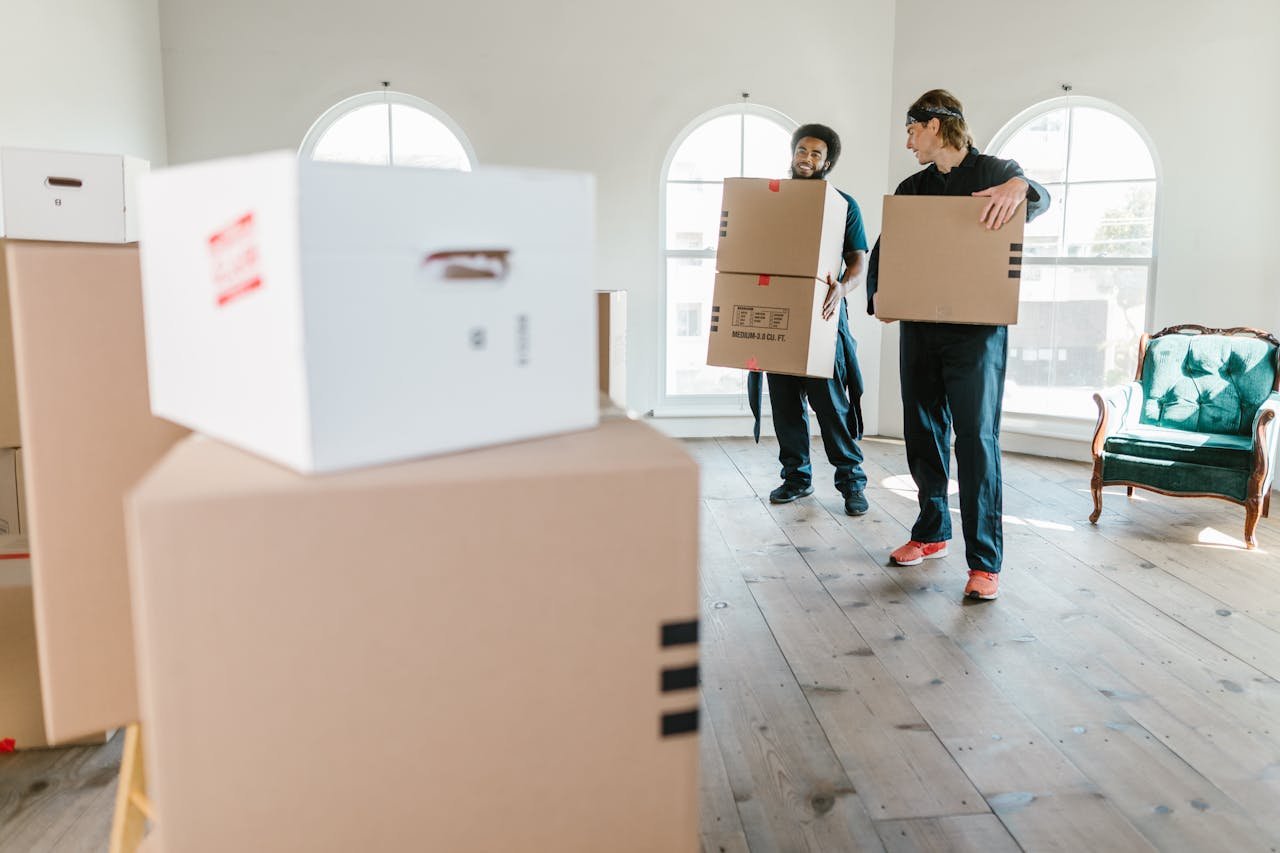 About Two movers in uniform carrying boxes in a bright, new home setting.